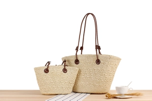 Detail of straw woven tote set with brown leather handles on a natural wooden table