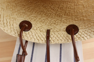 Detailed close-up of straw woven tote handle with brown faux leather stitching