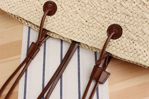 Detail of hand-woven straw bag featuring a brown leather strap and reinforced stitching