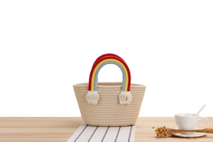 Detail of handmade cotton rope bag with colorful rainbow handle and white tassel pom-poms