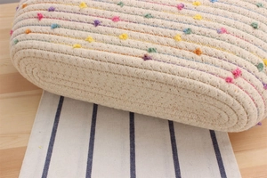 Détail du sac de plage en corde de coton tissée avec des pompons colorés sur une table en bois