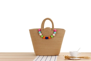 Détail du sac tissé en coton kaki avec pompons colorés posé sur une table en bois