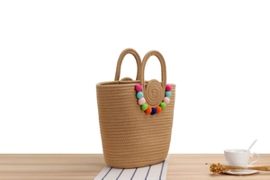 Détail d'un sac cabas tissé avec pompons colorés et poignée circulaire intégrée