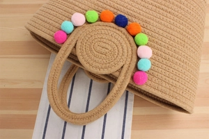 Détail du sac bohème en corde de coton avec pompons colorés sur un fond en bois naturel