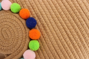 Gros plan d'un sac tissé en corde de coton avec pompons colorés et texture spirale
