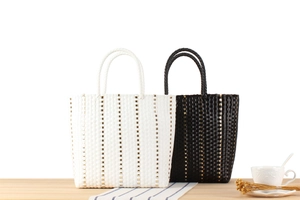 Détail de sacs cabas tissés en noir et blanc avec accents dorés sur une table en bois
