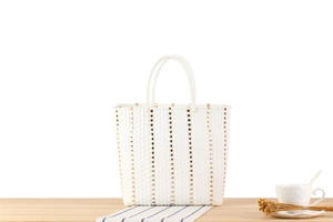 Détail du sac cabas tressé blanc avec accents métalliques dorés sur surface en bois
