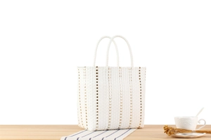 Détail du sac cabas blanc tressé avec clous métalliques dorés sur une surface en bois