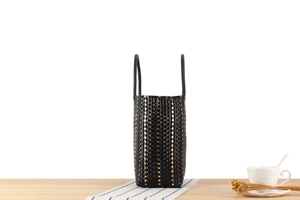 Détail du sac cabas tissé noir avec rayures dorées posé sur un bureau en bois rustique