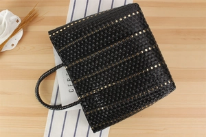 Détail du sac cabas tissé noir avec accents métalliques dorés sur un bureau élégant