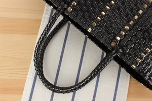 Détail d'un sac de plage noir tressé main avec boucles dorées et poignées arrondies