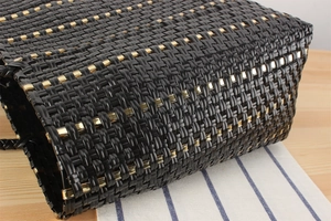 Détail d'un sac cabas tressé noir avec des rayures métalliques dorées sur une table en bois