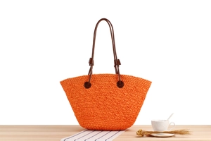 Detailed texture of hand-woven bright orange tote bag with brown leather shoulder straps