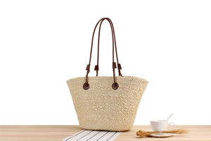 Detail of cream woven tote bag with brown handles on a minimalist wooden surface