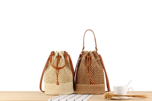 Close-up of woven drawstring bucket bags in beige and camel with brown leather straps