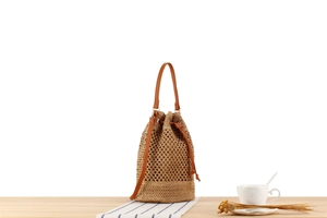 Detail of hand-woven straw bucket bag with brown leather drawstring and strap on a table