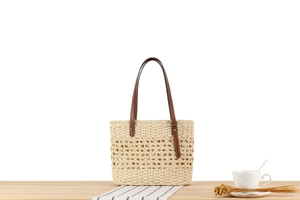 Detailed view of hollow-out straw tote with leather handles on a rustic table