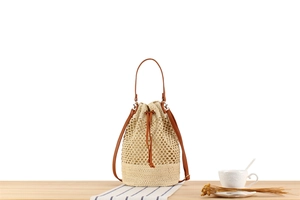 Close-up of beige woven bucket bag with brown leather drawstring and straps on wooden table