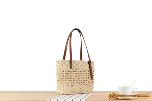 Detailed close-up of a woven paper rope beach bag with dark brown leather handles