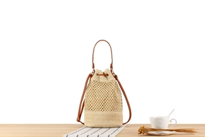 Detail of straw bucket bag featuring intricate cutout weave and brown leather drawstring