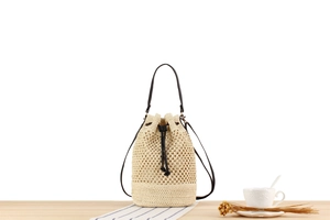 Detail of woven straw bucket bag with black leather drawstring and golden hardware
