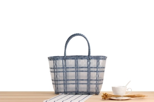 Blue and white checkered hand-woven plastic tote bag displayed on a light wooden table