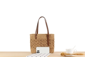 Detail of a beige woven tote bag with brown straps compared to a smartphone for size