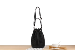 Detail of black woven bucket bag with drawstring closure and leather strap on a table