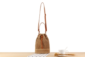 Macro detail of bohemian straw bucket bag with woven texture and leather strap on a table