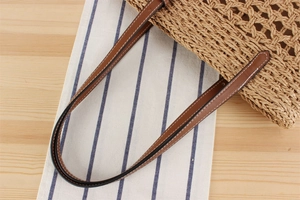 Detail of brown leather straps with white stitching on a woven straw beach tote bag