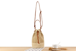 Detail of woven straw bucket bag showing textured mesh and brown leather drawstring strap