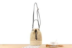 Detail of beige woven bucket bag with black drawstring closure and leather shoulder strap