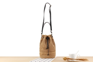 Detail of khaki woven bucket bag featuring black leather straps and drawstring closure