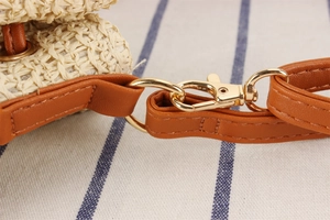 Detail of woven straw bucket bag with brown leather strap and golden metal lobster clasp