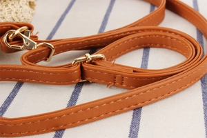 Detail of brown leather shoulder strap with gold metal hook on woven bucket bag