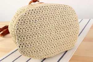 Macro detail of beige woven straw bucket bag with brown leather strap on striped cloth