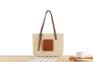 Detailed shot of woven straw tote bag with brown leather patch on wooden surface