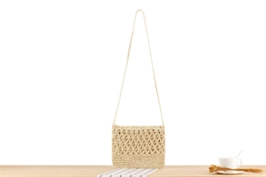 Close-up of cream hollow floral knit straw shoulder bag on a light wooden table