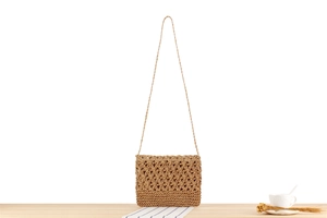 Close-up of vintage hollow floral woven shoulder bag on light wood surface with coffee cup