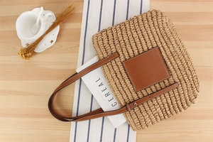 Top view of a large woven straw tote bag with brown leather handles on a wooden table