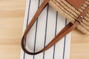 Detail of straw woven tote bag featuring brown leather strap and neat stitching