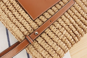 Close-up of beige woven straw tote with brown leather strap and white stitching details
