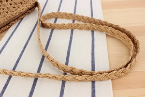 Detail of hand-woven paper rope shoulder strap and zipper closure on a straw tote bag