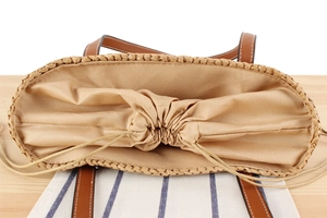 Detail of woven straw tote bag with brown leather handles and drawstring inner lining