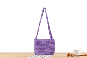 Detailed texture of purple hand-woven cotton rope shoulder bag on a bright wooden table