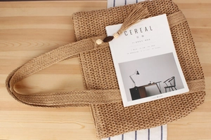 Detail einer handgewebten Strohtasche mit Holzperlen und Quasten auf einem Holztisch
