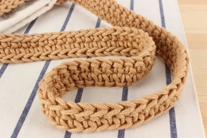 Close-up of a hand-woven cotton rope shoulder strap in khaki on a striped linen fabric