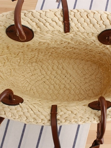 Straw woven tote bag with brown leather handles and spacious interior for beach vacations