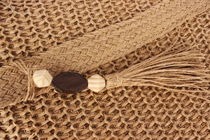 Detail einer Strohtasche mit dekorativen Holzperlen und einer feinen Quastenverzierung