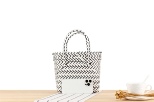 Mini hand-woven striped plastic tote bag with phone for scale on wooden table